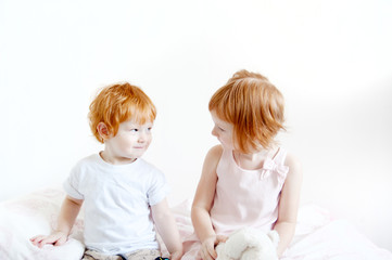Red-haired brother and sister are sitting on the bed