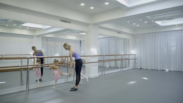 The trainer teaches two girls how to turn around beautifully while ballet class. The teacher showes how to stand on the tips of the toes straight, raises her arms upward and twist right. The little