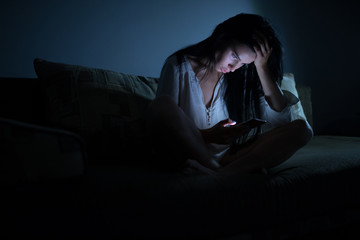 Tired woman using blue smartphone screen at night dark room