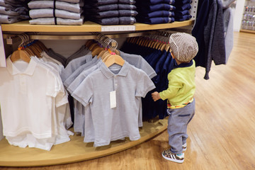 Cute little Asian 18 months / 1 year old toddler baby boy child choosing & buying kids clothes in garments shop,