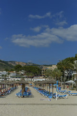 the view of the sun loungers and parasols on the sandy beach on background of mountains and blue sky