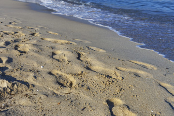 fragment of sandy beach with footprints in the sand with a moving sea waves closeup