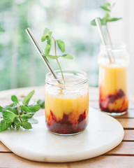Summer mango orange juice smoothie with red fruit and mint, nice bokeh background with greens