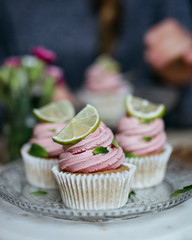 Strawberry and lime vegan cupcakes, one in center, woman in background enjoying cupcake, flowers