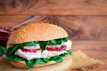 Healthy burger with boiled chicken, berry jam and fresh spinach. Easy and wholesome chicken burger on a wooden board. Rustic style