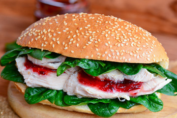 Boiled chicken breast, berry jam and fresh spinach burger. Simple and healthy chicken burger on a wooden board. Closeup