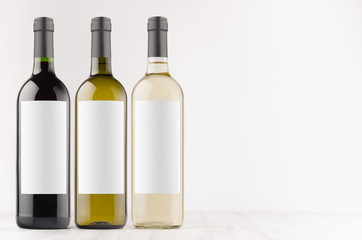 Wine bottles collection - transparent, green, black- with blank white labels on white wooden board, mock up, copy space. Template for advertising, design, branding identity.
