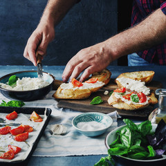Obraz na płótnie Canvas Man preparing Italian bruschetta with baked tomatoes, basil and cheese