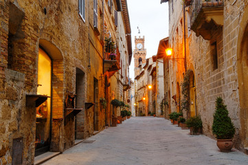 Pienza, Tuscany, Italy - ancient street with stone buildings, on background the city hall bell tower