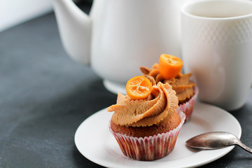 A teapot, a cup of tea and a caramel cupcake.