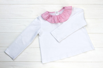 Pajama jacket on wooden shelf. Lightweight garment with beautiful collar. Girls' style, white and pink.