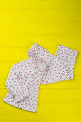 Folded pajama set on shelf. Cute floral sleeping garments for little girl. Studio shot with yellow wooden background.
