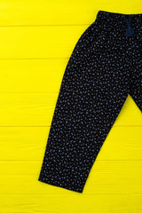 Fashionable floral pants on yellow background. Black loose garment with elastic waistband. Bright shot of girls apparel item.