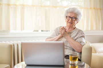 Emotional senior woman having video call with grandchildren via laptop. - obrazy, fototapety, plakaty