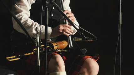 Fototapeta na wymiar Bagpipe player in a kilt plays musical instrument at the stage