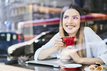 Beautiful young woman smiling and having coffee in a cafeteria