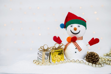 Christmas concept background of Design Snowman with shiny gift box and pine cone on white snow over blurred light bokeh on white background