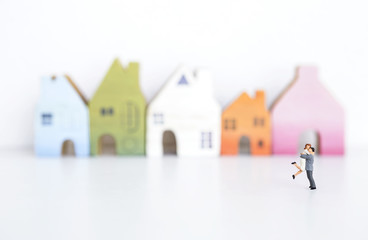 Happy miniature couple over blurred colorful wooden house on white background, estate and property business concept