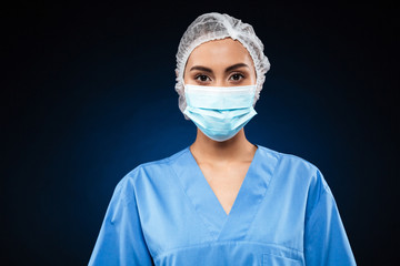 Young doctor in medical mask and cap looking camera