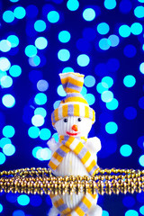 Snowman toy and golden beads on a glass table with a beautiful blue bokeh - 184251499