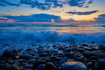 Beautiful sunset with blue wave and moist stones