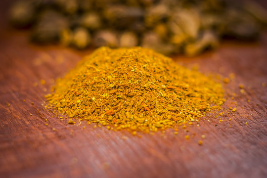 Raw black cardamom with its powder on a brownish wooden surface.
