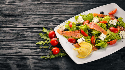 Salmon salad, feta cheese, salad leaves and fresh vegetables on the plate. On a wooden background. Top view. Free space for text.