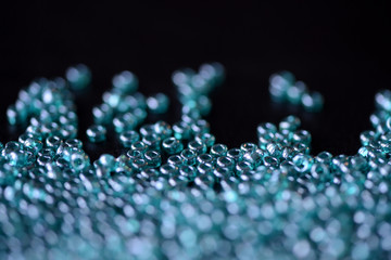 Scattered seed beads aquamarine color on a dark surface close up