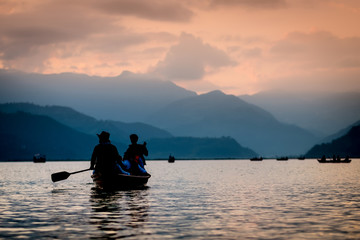 Silhouettes of people on boats at sunset on Phewa lake. Vanilla sky and mountain background. - obrazy, fototapety, plakaty