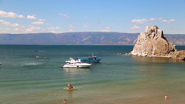 View of the Baikal Bay Shamanka in summer day. Ships and yachts. Tourists swimming in bay in sunny summer day. Olkhon Island, Baikal, Russia, Siberia.