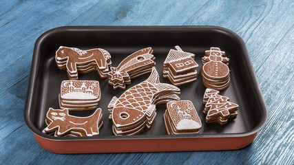 Hand-decorated Christmas gingerbreads stacked on baking sheet. Ornate pastry of various shapes like fish, snowman, cat, cottage or Bethlehem star.