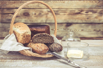 Various wheat and rye bread in a basket. Bread, table knife and butter. Healthy breakfast concept. Easy toning. Wooden background