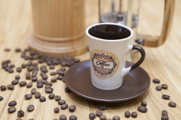 A cup of fresh coffee on a table. Spilled coffee beans and a background coffee maker.