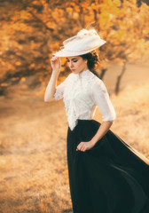 Exquisite lady in a vintage dress in a beautiful hat walks among the hills, against the background...