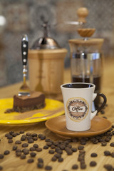 A cup of coffee and a piece of cake placed on a table with a coffee maker in the background