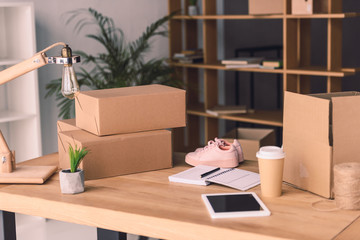 freelance worker workplace with cardboard boxes, notebook and pair of shoes at home office