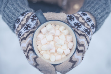 hands of the girl holding a mug with hot chocolate on the background of snow