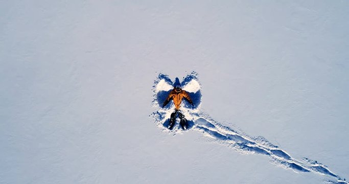 Vue rapproch&eacute;e d'un homme qui souri en r&eacute;alisant un ange allong&eacute; dans la neige - orange manteau montagne sourire bouge r&eacute;flection hiver
