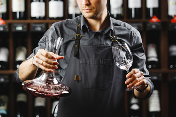 Barman in apron holds vessel with red wine and glass