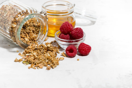 sweet granola in a jar, fresh raspberries and honey on white table, closeup