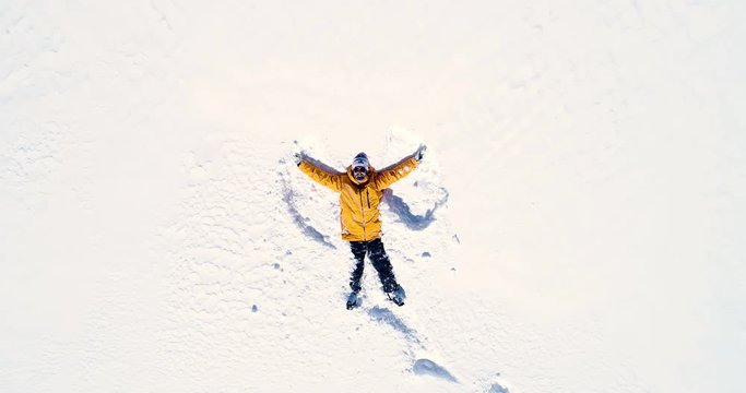 Vue rapproch&eacute;e d'un homme qui souri en r&eacute;alisant un ange allong&eacute; dans la neige - orange manteau montagne sourire bouge r&eacute;flection hiver 