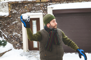 man with beard in gloves throws snowballs in yard