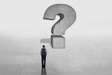 A small elegant business person in suit standing with his back in front of a huge question mark in...