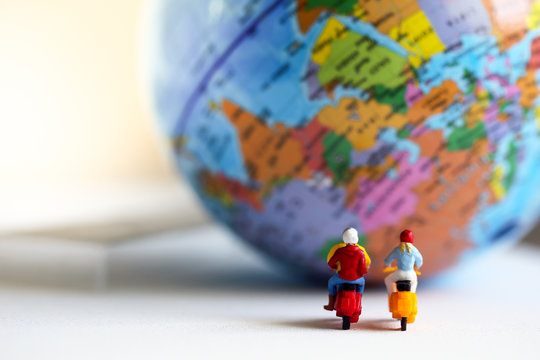 Group of traveler miniature people figures ride motorcycle / scooter to world map.