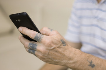 Old man with tattooed hands using a black smartphone, close-up