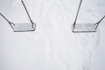Empty swings with snow/Pair of chained rubber swings covered with fresh snow and hanging above the snow layer.