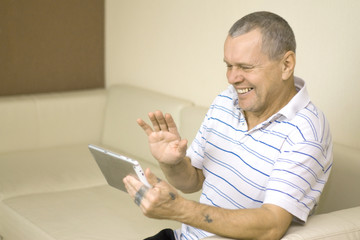 Old man with tattooed hands using tablet PC waving hello having a video conference