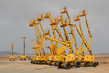 Several colorful self propelled wheeled hydraulic articulated boom lifts with telescoping boom and yellow basket on a desert landscape background © Arkadii Shandarov