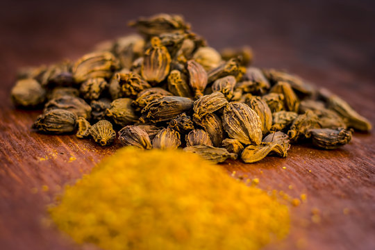 Raw black cardamom with its powder on a brownish wooden surface.