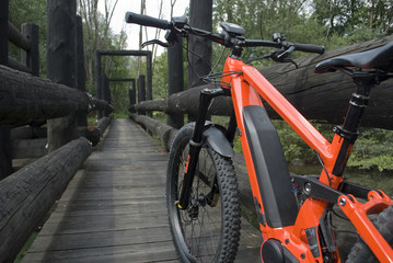 Panorama: Ebike E-bike electric bicycle orange, detail from back, leaning on an old dark wooden...